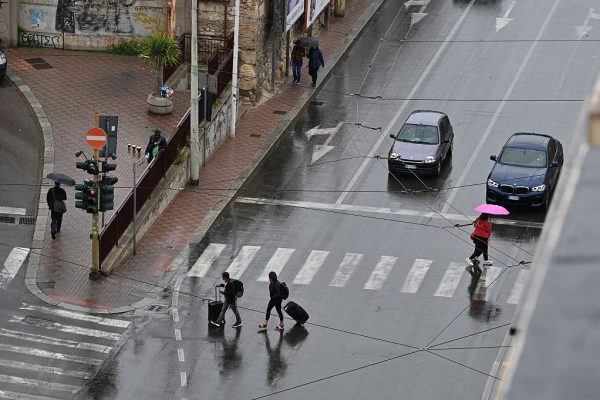 CAGLIARI, SARDINIA - APRIL 28: People cross the road at a zebra crossing holding umbrellas and pushing luggage in the rain on April 28, 2025 in Cagliari, Italy. (Photo by John Keeble/Getty Images)